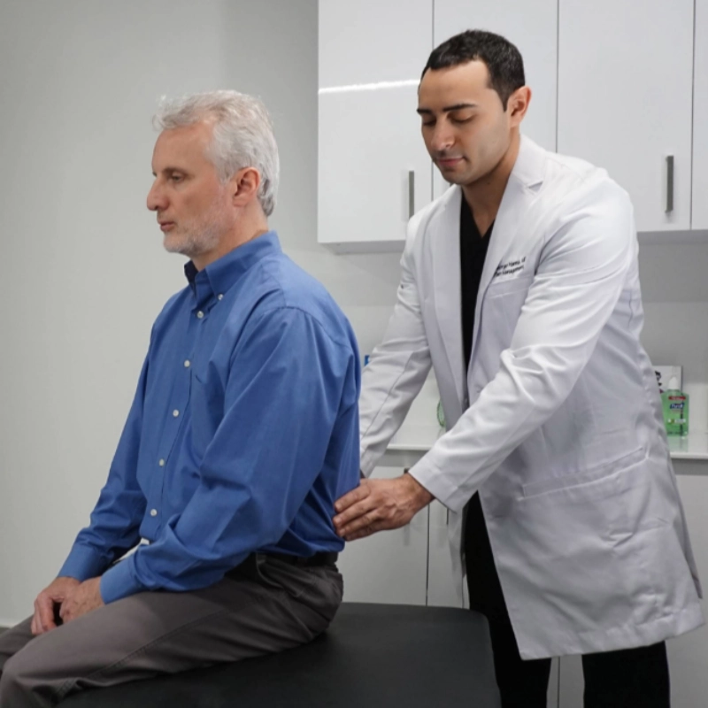 A friendly doctor in a white lab coat shows information about a vein treatment process on a tablet to a seated, smiling patient in a modern medical office setting.