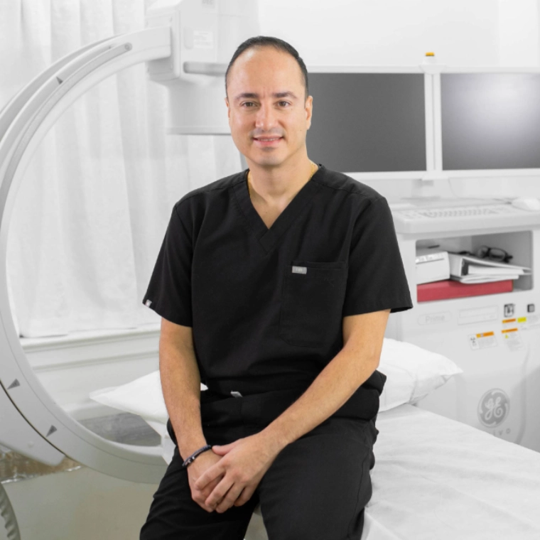 A friendly doctor in a white lab coat shows information about a vein treatment process on a tablet to a seated, smiling patient in a modern medical office setting.