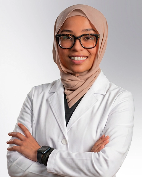 Professional headshot of Dr. Anee Khan wearing a white lab coat, smiling at the camera against a grey background. This is a standard medical professional portrait used for clinic or practice identification.