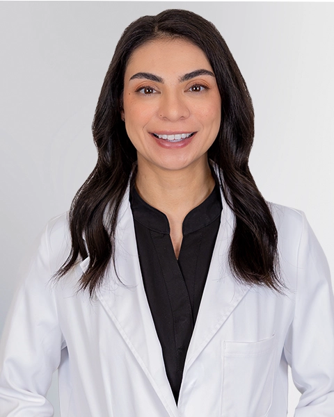 Professional headshot of the Advanced Practice Provider Dominique Lekander wearing a white lab coat, smiling at the camera against a grey background. This is a standard medical professional portrait used for clinic or practice identification.