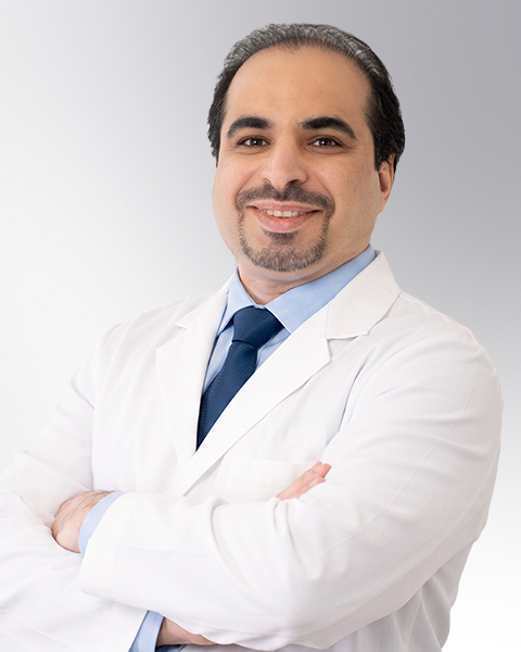 A healthcare provider stands against a neutral background, wearing a white medical coat. He has a calm and approachable expression, and his arms are gently crossed. The image conveys confidence, professionalism, and warmth suitable for a clinical setting.