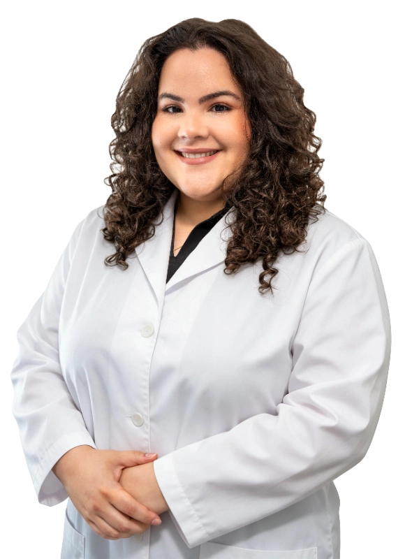 Professional portrait of Dr. Hanen Fernandez, MD, a healthcare provider wearing a white lab coat over dark scrubs, photographed against a black background. Dr. Fernandez has long curly brown hair and presents a warm, approachable smile with hands clasped in front, exemplifying the professional demeanor expected of medical staff specializing in interventional procedures.