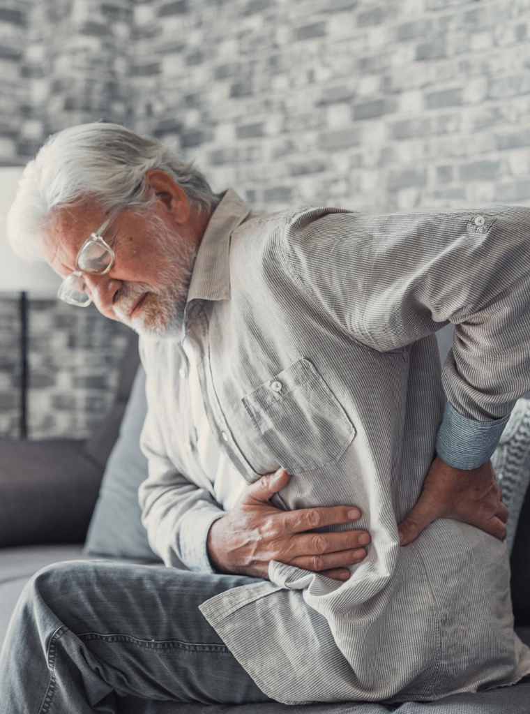 Hip_pain_condition_optimized An elderly man sitting on a couch, holding and hip in pain.