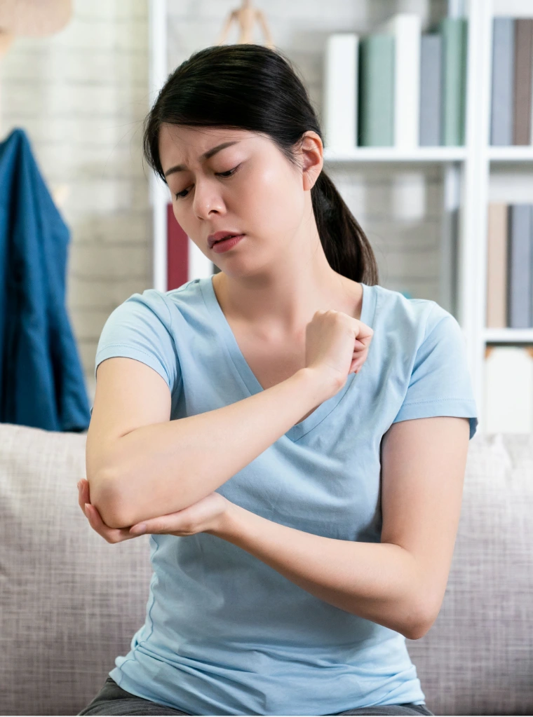 Joint_pain_condition_optimized A woman sitting indoors holding her joint in pain.
