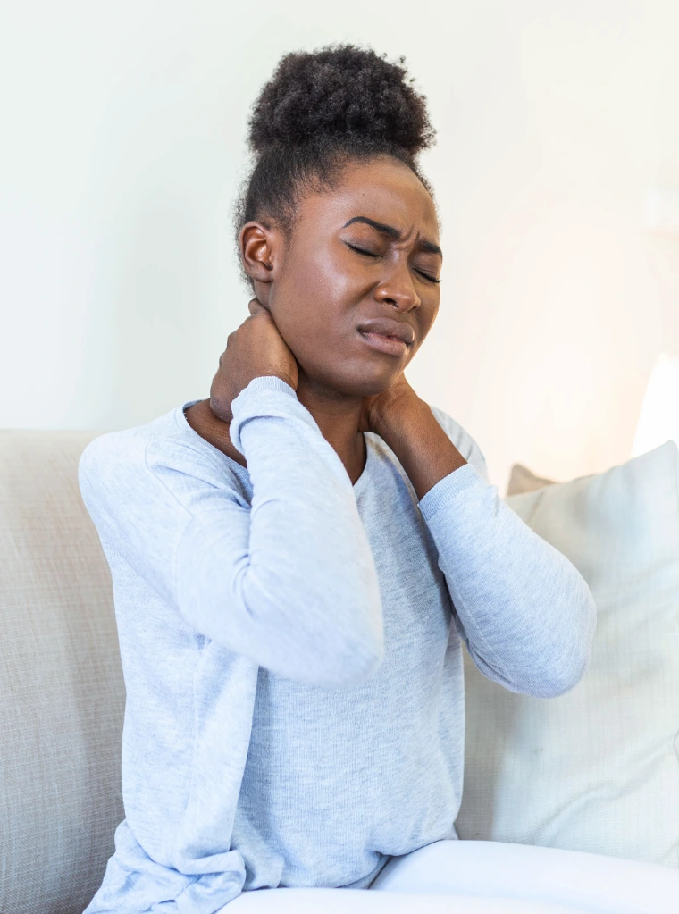 Neck_Pain_condition_optimized A woman sitting on a couch holding the back of her neck in pain.