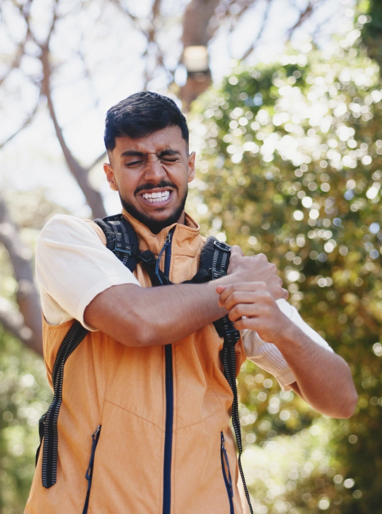 Shoulder_pain_condition_optimized A man wearing a backpack holding his shoulder in pain outdoors.